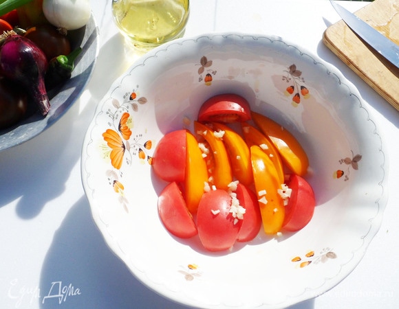 Моем и очищаем овощи. Помидоры нарезаем крупными дольками примерно на 6 частей и выкладываем на дно миски. Посыпаем мелко нарезанным чесноком.