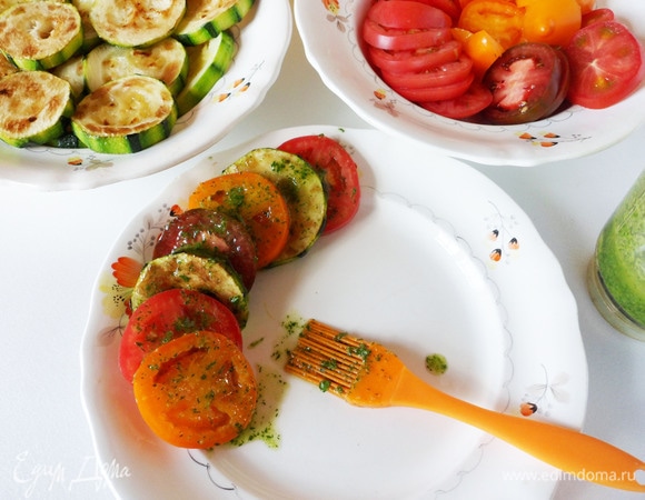 В измельчитель или кухонный комбайн загрузите очищенный чеснок, рубленую кинзу (можно заменить на петрушку и/или укроп), влейте белый винный уксус (можно заменить на яблочный) и растительное масло. Измельчите до однородности. Если нет измельчителя, можно обойтись и без него. В таком случае мелко нарежьте все ингредиенты и смешайте их в миске. Теперь выложите кружочки кабачков с помидорами, смазывая или поливая их заправкой.