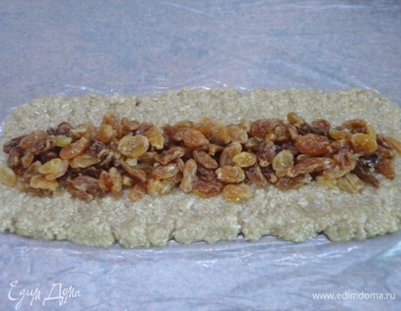 Тесто и изюм разделите на три части. Каждую часть руками распределите в прямоугольники (примерно 12х35 см). Удобнее это делать сразу на пищевой пленке. Выложите изюм и с помощью пленки соедините края. Закатайте каждый рулет полностью пленкой и слегка прокатайте по столу, чтобы скрепить срез. Уберите тесто в холодильник на 2 часа или в морозильную камеру на 30 минут.