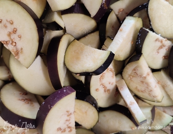 Баклажаны разрезать вдоль пополам и каждую половинку нарезать на дольки. Сложить в миску, посолить и оставить на 20 минут.