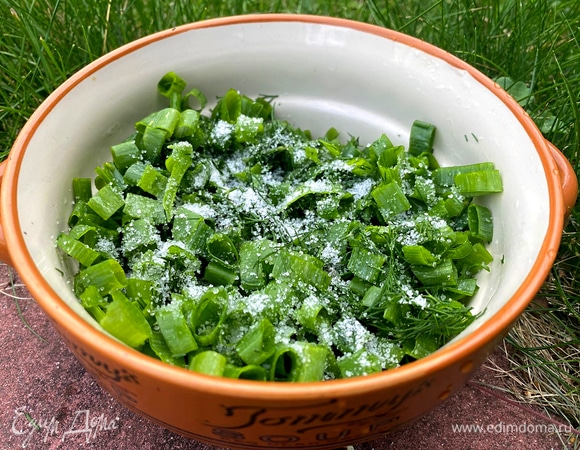 Нарежьте мелко укроп и лук, переложите в отдельную емкость, посыпьте солью и помни́те ложкой — зелень даст сок и окрошка с помидорами получится еще вкуснее. 