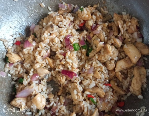 Через 1 минуту добавляем рис. Все перемешиваем, разбивая комочки риса (если образовались), добавляем 3 столовые ложки соевого соуса и 1 столовую ложку рыбного. Хорошо перемешиваем и жарим минуту.