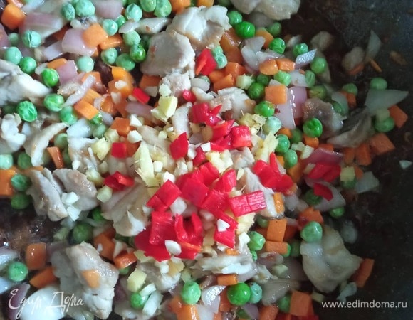 Добавляем лук, морковь и зеленый горошек. Через 3 минуты добавляем чеснок, имбирь и перец чили. Жарим 1 минуту, постоянно помешивая. Все обжаривается на сильном огне.