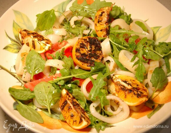 Готовых кальмаров нарезать кольцами и отправить к помидорам, все перемешать, полить заправкой и украсить карамелизированным лимоном.