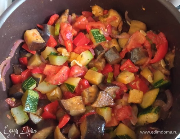 Через пару минут добавляем помидоры. Помидоры и перец можно очистить от кожуры. Через минуту добавляем обжаренные баклажаны. Добавляем молотый кориандр и хмели-сунели. Накрываем крышкой и тушим на медленном огне 20–25 минут. Солим по вкусу.<br />
Шинкуем чеснок и кинзу. Можно посыпать ими готовое блюдо, я же добавляю при готовке. Через минуту выключаем, и блюдо готово! Приятного аппетита!