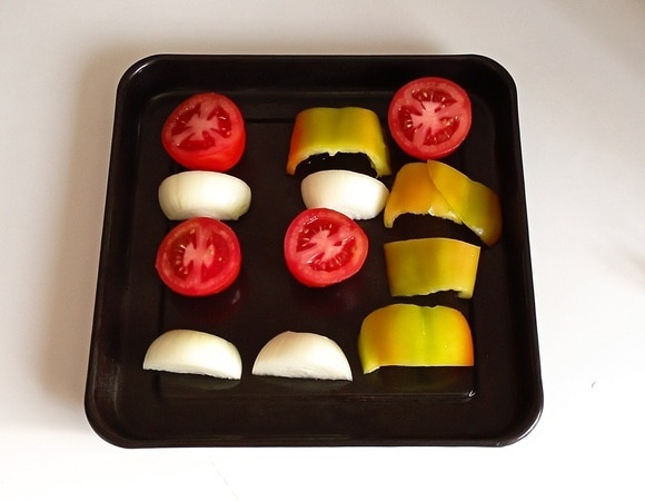 У помидор аккуратно удалить плодоножку и разрезать их пополам. Репчатый лук разрезать пополам, а затем еще раз пополам. Перец очистить от семян и затем разрезать, как и репчатый лук. После чего смазать противень растительным маслом и выложить на него нарезанные овощи. Разогреть духовку до 195°C и поставить в нее противень с овощами на 25 минут. Далее вынуть противень и остудить овощи.