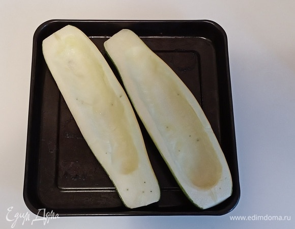 Половинки кабачка чуть посолить. Смазать противень растительным маслом и положить на него кабачок. Запекать в разогретой до 190°C духовке 20 минут.<br />
Пока кабачок запекается, нужно в течение 10–15 минут отварить шампиньоны в 1 литре кипящей подсоленной воды. Затем слить воду и остудить шампиньоны, разрезать пополам.