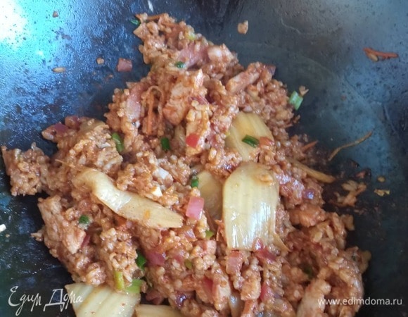 Добавляем ветчину. Жарим 2 минуты. В некоторых рецептах к луку сначала добавляют ветчину, а потом кимчи. Я пробовала и так, и так. Особой разницы не вижу. Жарим еще минуту, добавляем чеснок и зеленый лук, перемешиваем, добавляем сахар и острый перец, перемешиваем, обжариваем 30 секунд и добавляем отваренный рис. Все перемешиваем.<br />
Добавляем соевый соус, перемешиваем и добавляем (по желанию) кунжутное масло. Перемешиваем, жарим минуту и выключаем плиту. Жарим по яйцу на каждую порцию. У меня куда-то потерялась фотография с жареными яйцами. Извините. Но, думаю, пожарить яйца не составит труда никому.