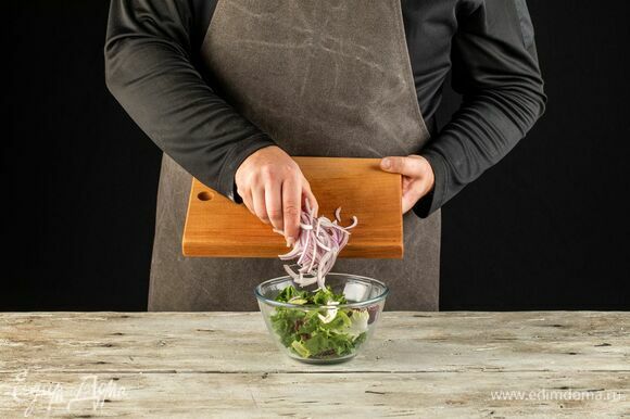 В салатник выложите салатный микс. Красный лук нарежьте перьями, добавьте к салату.
