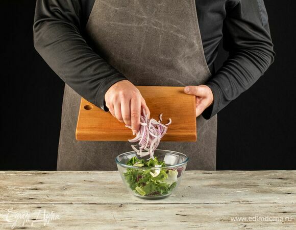 В салатник выложите салатный микс. Красный лук нарежьте перьями, добавьте к салату.