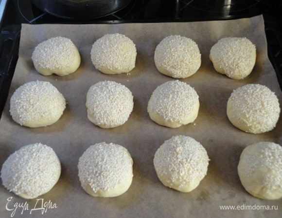 Каждую булочку обмакните в сироп, затем — в кунжут, выложите на противень и оставьте для расстойки на 30 минут. Включите духовку для разогрева на 180°C.