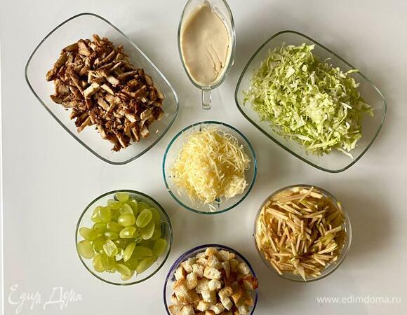 Нарезать капусту соломкой или кубиками. Куриные грудки — соломкой или кубиком, как нравится. Яблоко — соломкой или натереть на крупной терке. Виноград нарезать половинками, если с косточками, удалить их. Пармезан натереть на крупной терке. Приготовить домашние сухарики из белого батона.