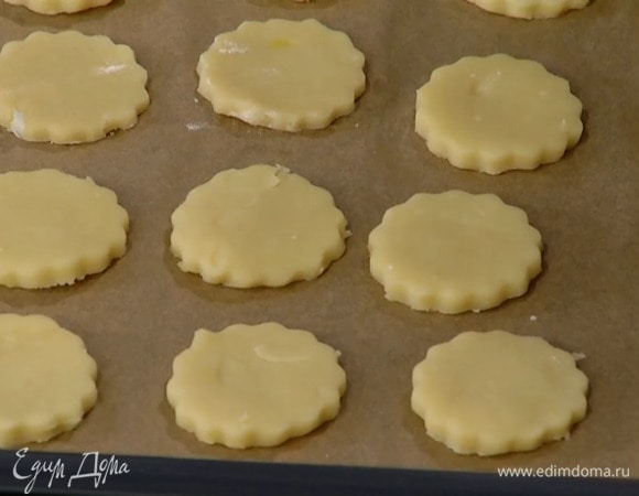 Половину охлажденного песочного теста перемешать с натертой цедрой, раскатать на посыпанной оставшейся мукой рабочей поверхности в тонкий корж. Вырезать из теста круглые лепешки, выложить на выстеленный бумагой для выпечки противень и выпекать в разогретой до 180°С духовке 8–10 минут.