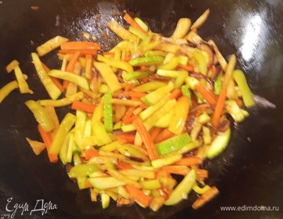 В вок добавляем масло. Кладем лук, обжариваем 1 минуту, добавляем морковь и сельдерей. Через 2 минуты — болгарский перец, еще через минуту — кабачок. Все обжариваем на сильном огне, постоянно помешивая, 3 минуты. Добавляем чеснок. Вливаем кунжутное масло. Жарим еще 1 минуту.