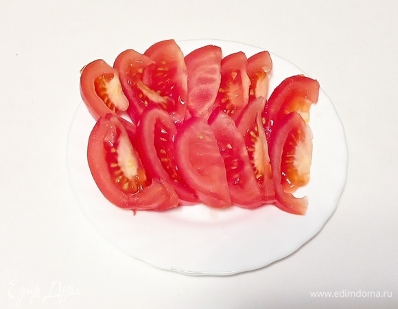 Помидор разрежьте пополал, а затем — тонкими дольками.