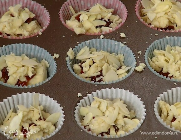 В формы для кексов вложить бумажные вставки и разложить тесто, наполняя их на половину объема. В каждую форму выложить по 1 ч. ложке джема, сверху разложить оставшееся тесто, посыпать миндальными лепестками.