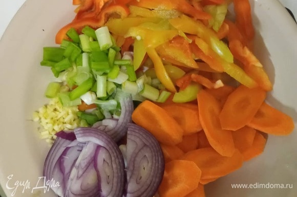 Подготовить овощи. Морковь нарезать тонкими пластинками, перец — полосками, лук — тонкими полукольцами, зеленый лук — кусочками по 2–3 см. Мелко порубить чеснок.