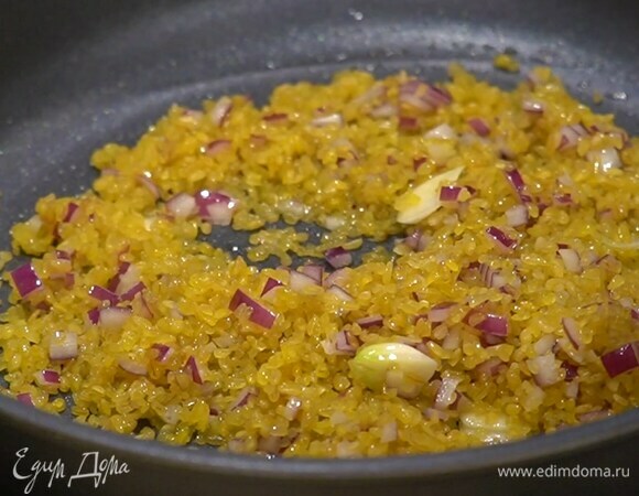 Разогреть в глубокой тяжелой сковороде оливковое масло и обжарить лук с чесноком, затем всыпать булгур и, помешивая, обжарить, чтобы крупа пропиталась ароматами.
