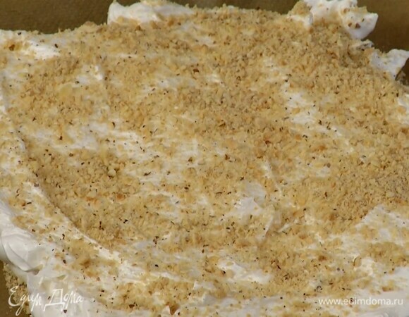 Застеленный бумагой для выпечки противень посыпать частью ореховой крошки, выложить белковую массу, разровнять и присыпать оставшимися измельченными орехами.