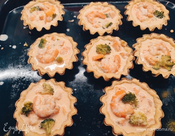 Для начинки размороженные креветки нарезать на несколько частей. Несколько штук можно оставить, чтобы положить сверху. Брокколи отварить в течение 5 минут, охладить и разделить на маленькие соцветия. Охлажденные тесто раскатать и выложить в формочки. Наколоть вилкой, накрыть бумагой, положить груз и выпекать 15 минут при температуре 180°C. Для заливки смешать яйцо и сливки. Посолить по вкусу. В тарталетки выложить креветки, брокколи, залить заливкой. Запекать еще 10 минут.