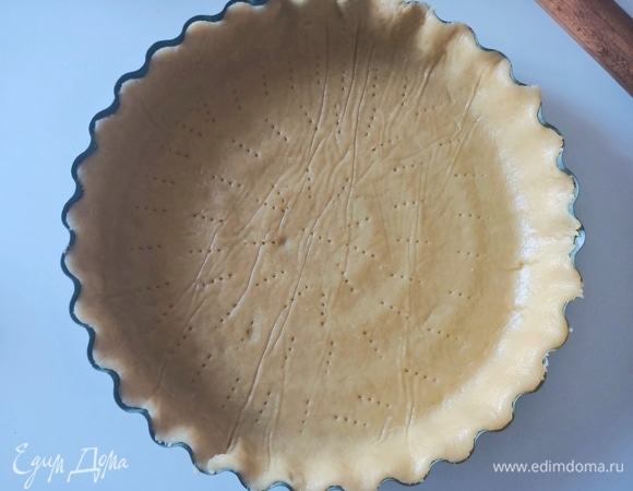 Достать тесто из холодильника, разделить его на две неравные части. Большую часть раскатать толщиной примерно 7–8 мм. Выложить в форму для кростаты диаметром 24 см. Сверху тесто наколоть вилкой.
