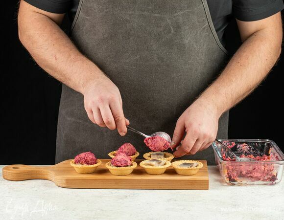 В каждую тарталетку положите пару кусочков сельди, репчатый лук. Сверху на лук в тарталетках выложите смесь из овощей.