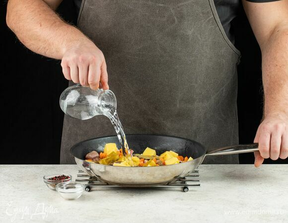 Влейте немного горячей воды, перемешайте и тушите на медленном огне до полной готовности картофеля.