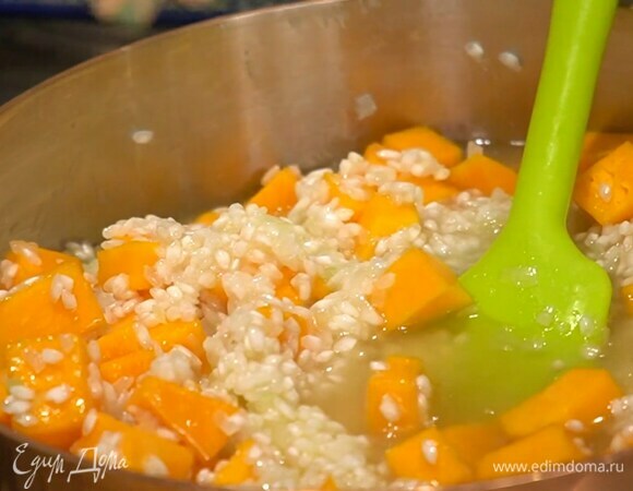 По паре половников вливать горячий бульон, перемешивая рис, в середине добавить тыкву.
