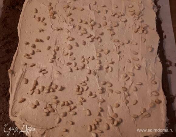 Взбейте охлажденный ганаш, добавив загуститель. Распределите его по бисквиту, оставив примерно 2 см с одного края. Посыпьте орешками.