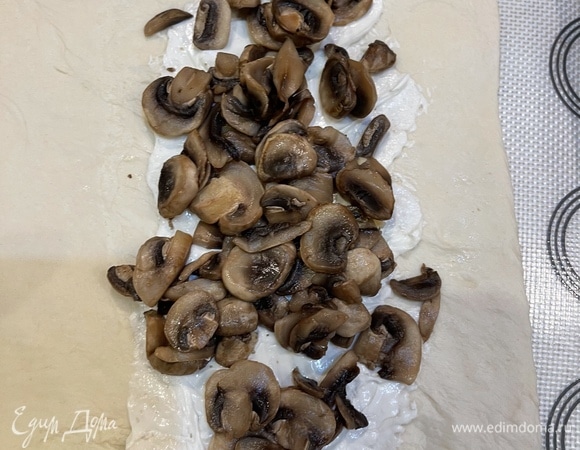 Слегка раскатываем тесто, смазываем сливочным сыром, сверху выкладываем шампиньоны. У меня было тесто в рулоне, я его разделила на 2 части и, соответственно, 2 пирога. Раскатываем тесто в прямоугольник и раскладываем начинку так, чтобы ее можно было укрыть свободной частью теста и слепить.