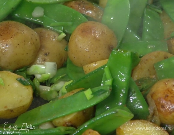 Зеленый лук нарезать наискосок и добавить к картофелю вместе с горошком, посолить и обжаривать еще буквально минуту.