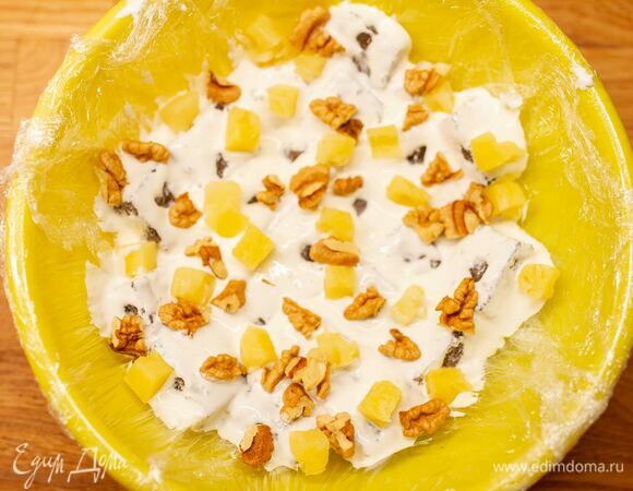 Взять большую чашу и застелить пищевой пленкой. Кубики теста обмакнуть в крем и выложить в чашу, в промежутках переслаивая орехами и ананасами. Таким образом собрать весь торт.