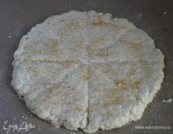 Тесто раскатать в круг диаметром 20 см прямо на пекарской бумаге. Острым ножом нарезать на 8 сегментов, но не прорезая до конца. Смажьте молоком или кефиром и посыпьте коричневым (или белым) сахаром.