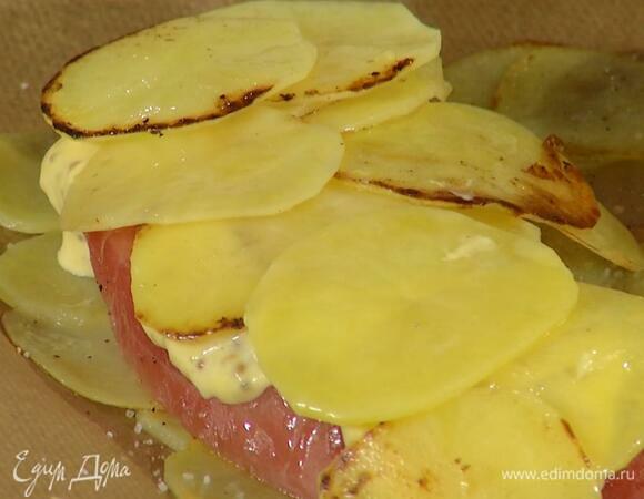 На выстеленный бумагой для выпечки противень в один слой уложить половину картофеля, на него поместить рыбу, смазать ее соусом, сверху выложить оставшийся картофель.