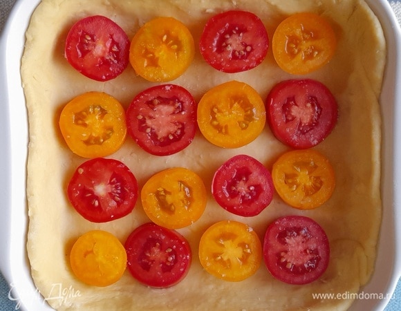 На тесто выложить часть кружков помидоров, чередуя по цвету.