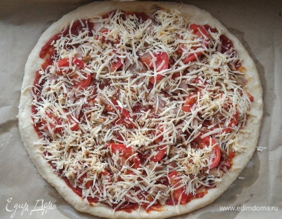 Посыпать заготовку приправами. Сыр натереть на мелкой терке и посыпать сверху. Сбрызнуть маслом от консервов. Поставить пиццу в духовку, предварительно разогретую до 200°С, на 15–20 мин. При выпечке ориентируйтесь на свою духовку.
