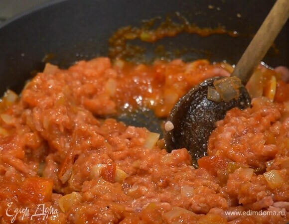Разогреть в сковороде оливковое масло и обжарить лук и чеснок до прозрачности, посолить и поперчить, добавить томатную пасту, консервированные помидоры, перемешать, выложить фарш, еще раз перемешать и на маленьком огне томить минут 10, до полуготовности.