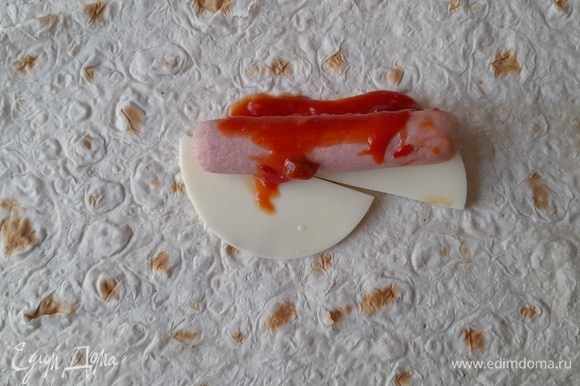На сыр положить сосиску, сверху полить 1 ст. л. острого томатного соуса (или кетчупа).