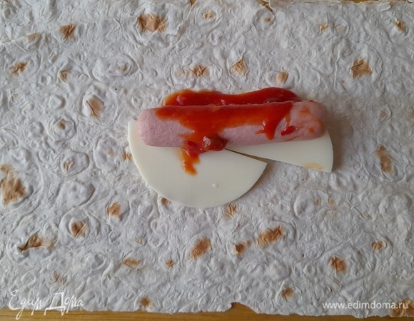 На сыр положить сосиску, сверху полить 1 ст. л. острого томатного соуса (или кетчупа).