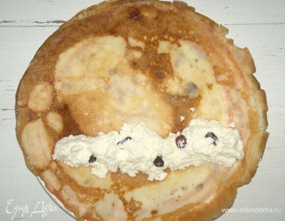 На тарелку выложить блинчик. Отступив с одного края блинчика 2–3 см, выложить немного творожной начинки в форме узкого цилиндра. Свернуть блинчик в рулетик. Начинить еще несколько блинчиков.