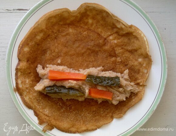 На более темную сторону блинчика с одного края выложить несколько столовых ложек начинки в виде полоски. На начинку разложить кусочки моркови и огурца.