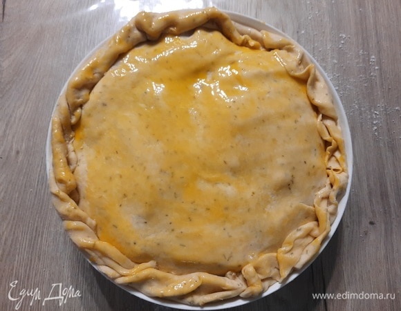 Раскатайте оставшееся тесто в круг по размеру формы и накройте им начинку. Защипните края. Смажьте верх желтком. Поставьте пирог в духовку и выпекайте 40–45 минут.