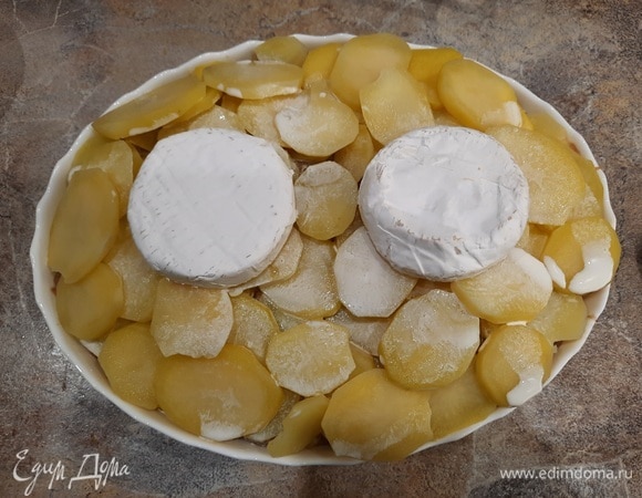 Добавьте вторую половину картофеля. Вылейте оставшиеся сливки и положите еще две половинки камамбера также корочкой вверх. Поставьте тартифлет в духовку и выпекайте 45 минут до появления румяной корочки.