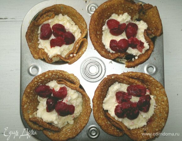 Формочки для кексов смазать тонким слоем растительного масла. В каждую формочку уложить рисовый блинчик, сделав две складки и придавая ему форму корзиночки. Затем выложить творожную начинку (примерно по 40 г), а также вишни без косточек, по 4–5 штук.