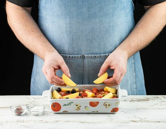 Переложите кролика вместе с маринадом в форму для запекания. По периметру выложите картофель, нарезанный дольками, посолите и поперчите его. 