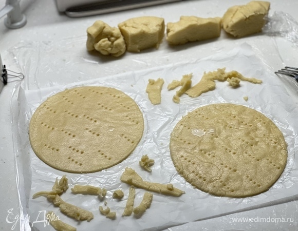 Разделить тесто на 6 частей. Раскатать каждую на пергаменте диаметром 19 см. Наколоть вилкой и выпекать при 200°C 5–7 минут до золотистости. Обрезки тоже испечь.