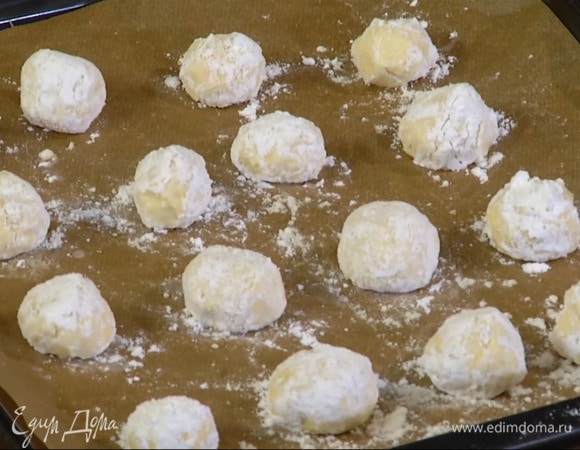Из охлажденного теста влажными руками скатать шарики диаметром 2 см, обвалять их в сахарной пудре и выложить на выстеленный бумагой для выпечки противень.