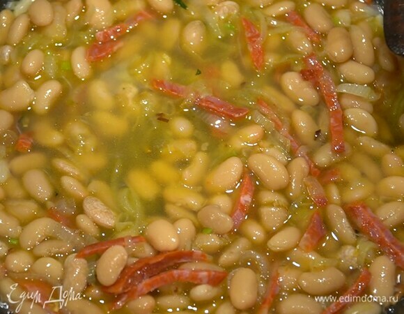 Оставшийся чеснок почистить, раздавить плоской стороной ножа и отправить к шалоту, добавить чоризо, отваренную фасоль, влить вино и дать алкоголю выпариться, затем прогревать все еще пару минут.