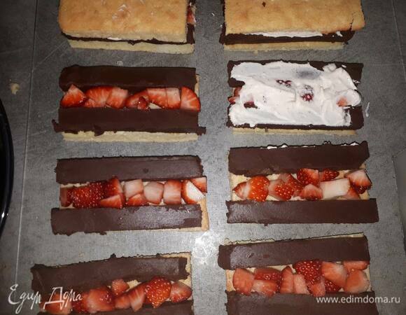 Нанесите тонкий слой белого ганаша на бисквит. Уложите по 2 брусочка черного ганаша по краям и кусочки клубники в центр.