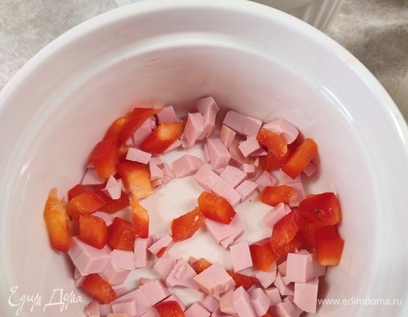 Колбасу и болгарский перец нарезать мелкими кубиками. Порционные формы для запекания смазать сливочным маслом и выложить в них начинку.